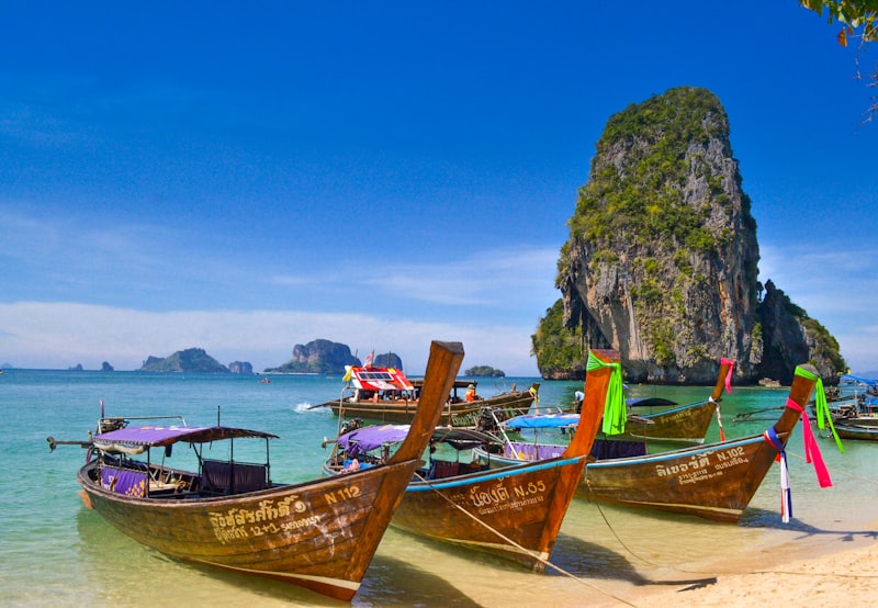 Long-tail boats on a turquoise beach in Thailand with limestone cliffs